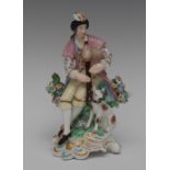 A Derby Patch Mark figure, of a man with bagpipes, seated wearing feathered headdress,