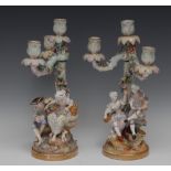 A pair of Dresden figural candelabra, of gallant and beau, both seated with birds, one with a nest,