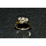 A diamond trilogy ring, three round brilliant cut diamonds linear set within a twisting surround,