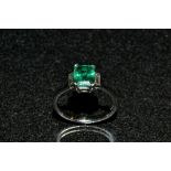 An emerald and diamond trilogy ring, central rectangular table cut emerald baguette, approx 1.