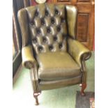 A wingback arm chair, green leather button upholstery.