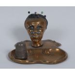 An Art Nouveau brass novelty pin cushion and thimble stand, as the head of a black woman,