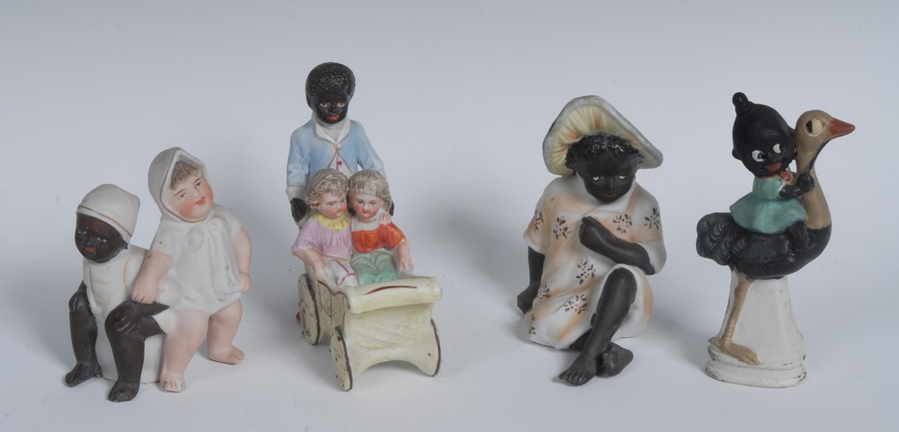 A 19th century German bisque porcelain model, of a black attendant pushing two children in a wagon,