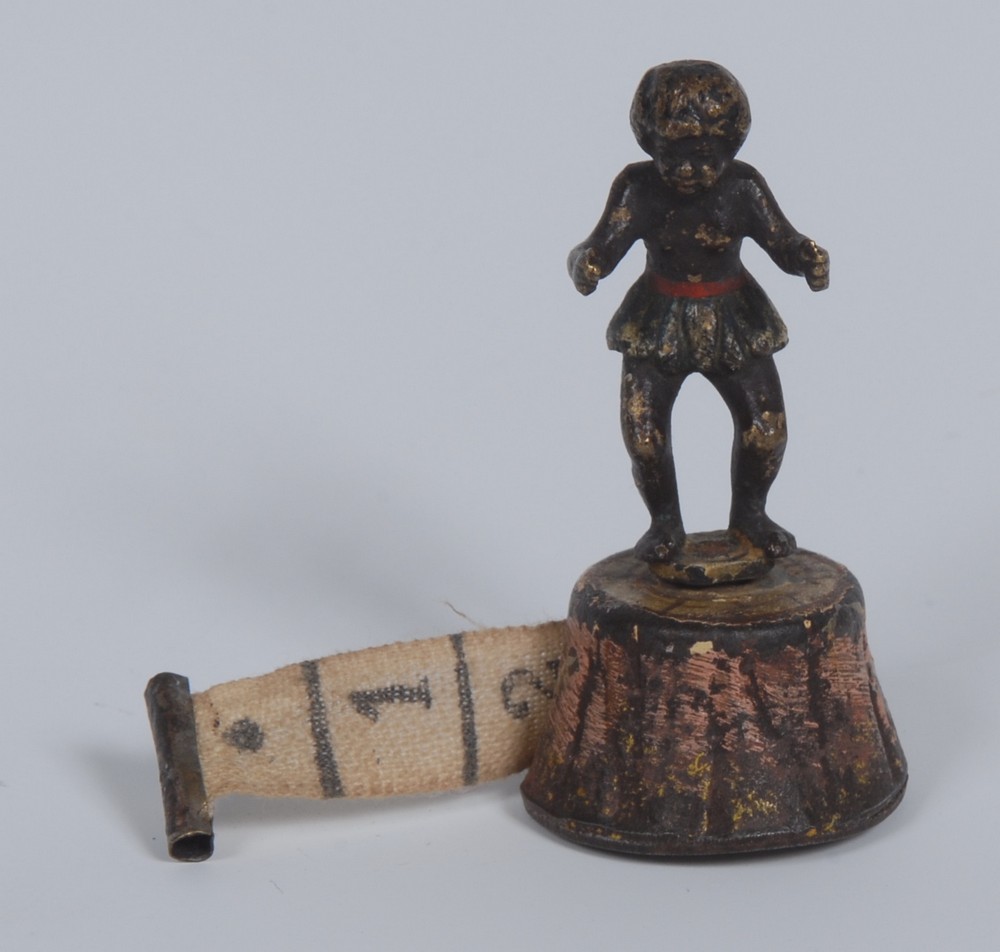 A late 19th century novelty tape measure, the winder as an african black boy, wearing a grass skirt,