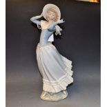 A Lladro figure of a young woman clad in elegant gown holding on to her hat,