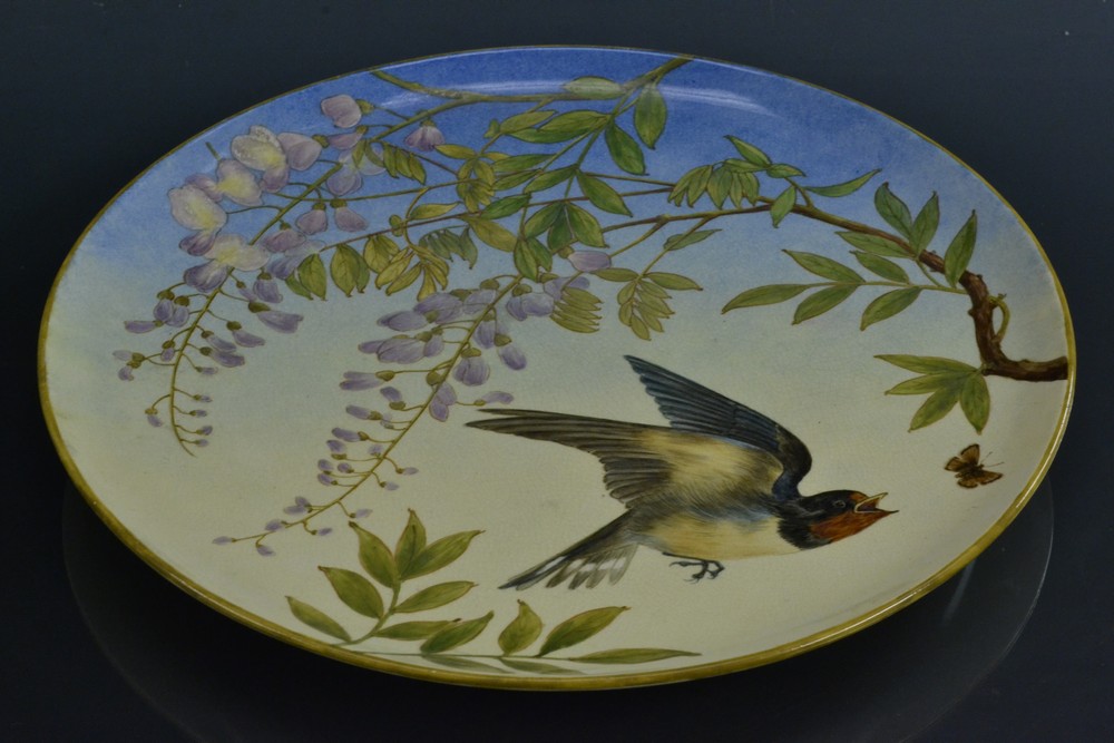 An Arts and Crafts circular wall plaque, hand painted by Rosa Vargas, signed, Wisteria and Swallow,