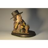 A 19th century papier mache inkwell, as a 17th century gentleman, seated, with quill in hand,