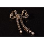 A diamond encrusted white metal ribbon bow brooch with pearl droplet terminals,