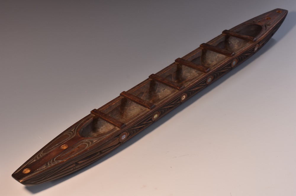 Tribal Art - a Maori model waka canoe, carved with stylised motifs and inlaid with abalone roundels,