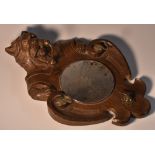 A Black Forest novelty mirror, carved as a dog peering over a shield shaped cartouche,