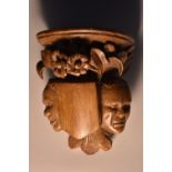 A Continental walnut bracket, carved in the manner of a medieval corbel with grotesque masks,