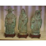 Three Chinese bronze immortals figures on timber stands, 25cm high approx