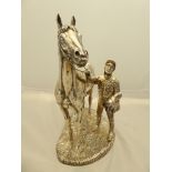 A Sterling Silver clad, filled sculpture of a race horse and dismounted jockey holding his saddle