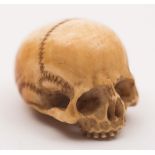 A Japanese carved ivory ojime: in the form of a miniature human skull, a hole for the cord,