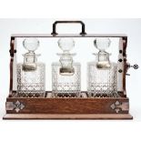 An oak and electro-plate mounted tantalus: containing three clear cut glass decanters and stoppers