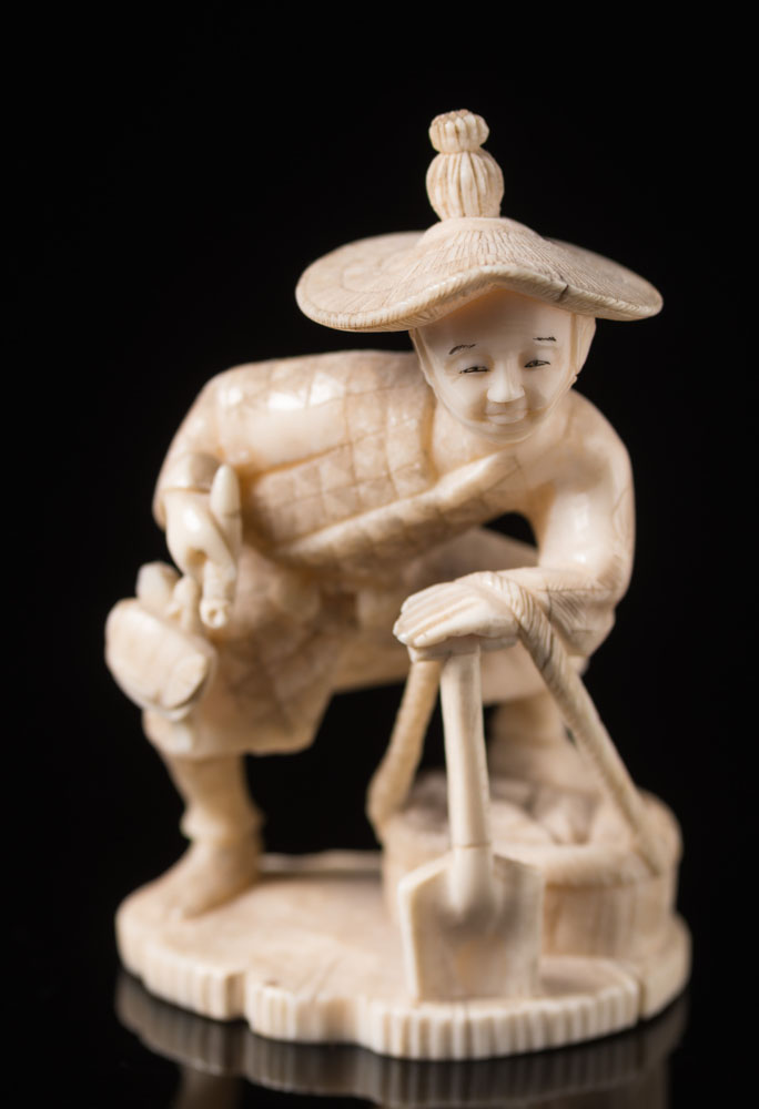 A Japanese carved ivory okimono: Meiji period (1864-1912) of a peasant wearing a straw hat,