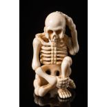 A Japanese ivory okimono: Meiji period (1864-1912), carved in the form of a seated human skeleton,