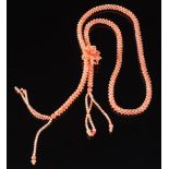 A pink coral bead rope necklace: with stylised floral cluster and two tassels.