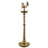 An Indian Deccan brass oil lamp: with cockerel finial and reservoir below,