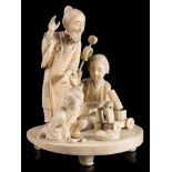 A Japanese carved ivory okimono of a mask maker and family: with wife and child kneeling on the