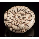 A Japanese carved ivory netsuke of a tiger: curled up, with inset eyes, having stained stripes,