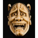 A Japanese carved ivory okimono of a Hannya Noh mask: with pierced eyes and nose, protruding horns,