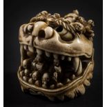 A Japanese ivory okimono in the form of a mythical beast's head: with a host of small figures on