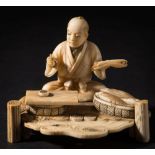 A Japanese carved ivory okimono of a scribe: seated by the riverside with a basket of fish by his