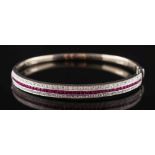 A ruby and diamond mounted hinged bangle: with central row of calibre-cut rubies estimated to weigh