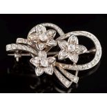 A diamond mounted floral spray brooch: with three flower heads and ribbon scroll pave-set with old