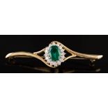 An emerald and diamond mounted bar brooch: the central oval emerald 10mm long x 8mm wide,
