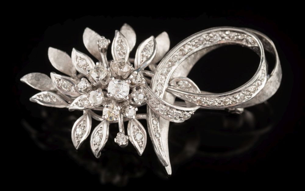 A diamond mounted floral spray brooch: of leaf and ribbon scroll design with circular brilliant-cut