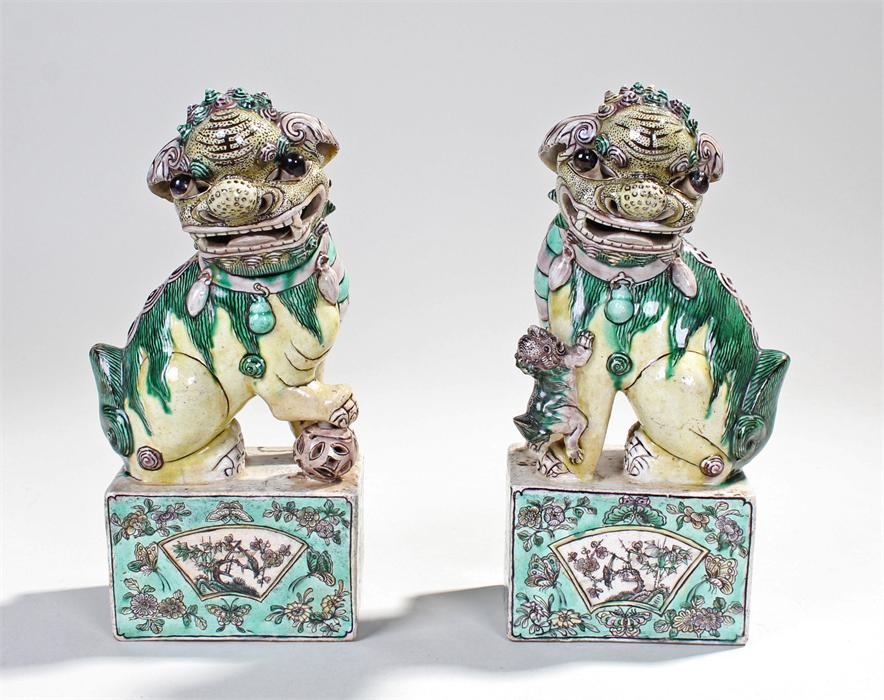 Pair of Chinese dogs of Fo, decorated in greens, yellows and violet, one standing on a ball the