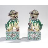 Pair of Chinese dogs of Fo, decorated in greens, yellows and violet, one standing on a ball the