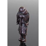 19th century finely carved wooden Japanese netsuke figure of a sennin, leaning on a staff his face