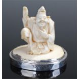 Japanese Meiji carved figural ivory, of a seated man holding up a hand, raised on a white metal