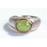 Silver and stone set ring, the pale green oval stone with yellow metal surround and tapering