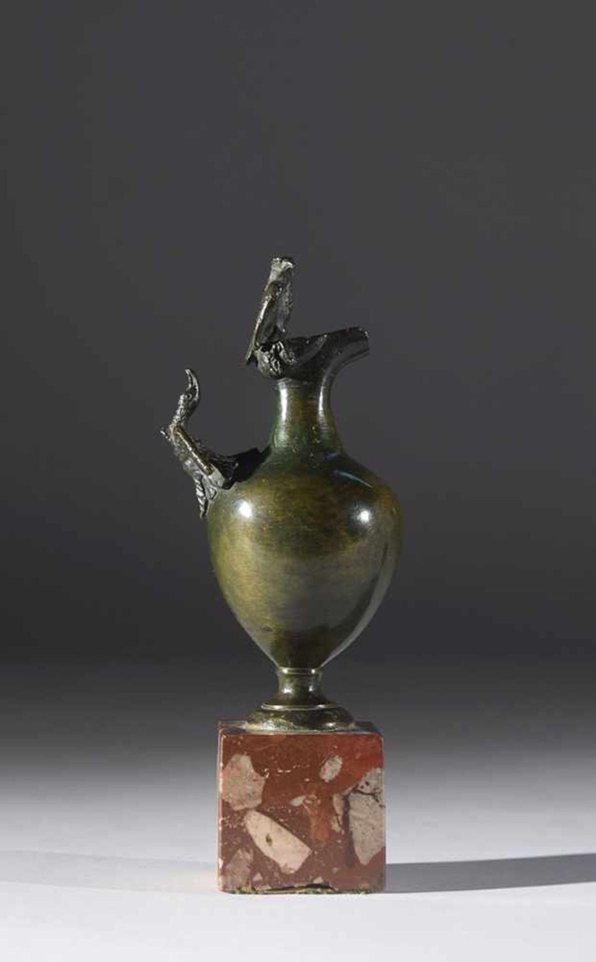 A small patinated bronze spout on a red marble base, 18th century, total height 21cm.