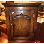 An 18th Century style oak corner cupboard with dentil moulded cornice, the ogee fielded panel door