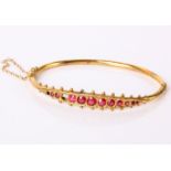 A 9ct gold bangle set with ruby coloured stones (two stones missing), 5.6g in total.