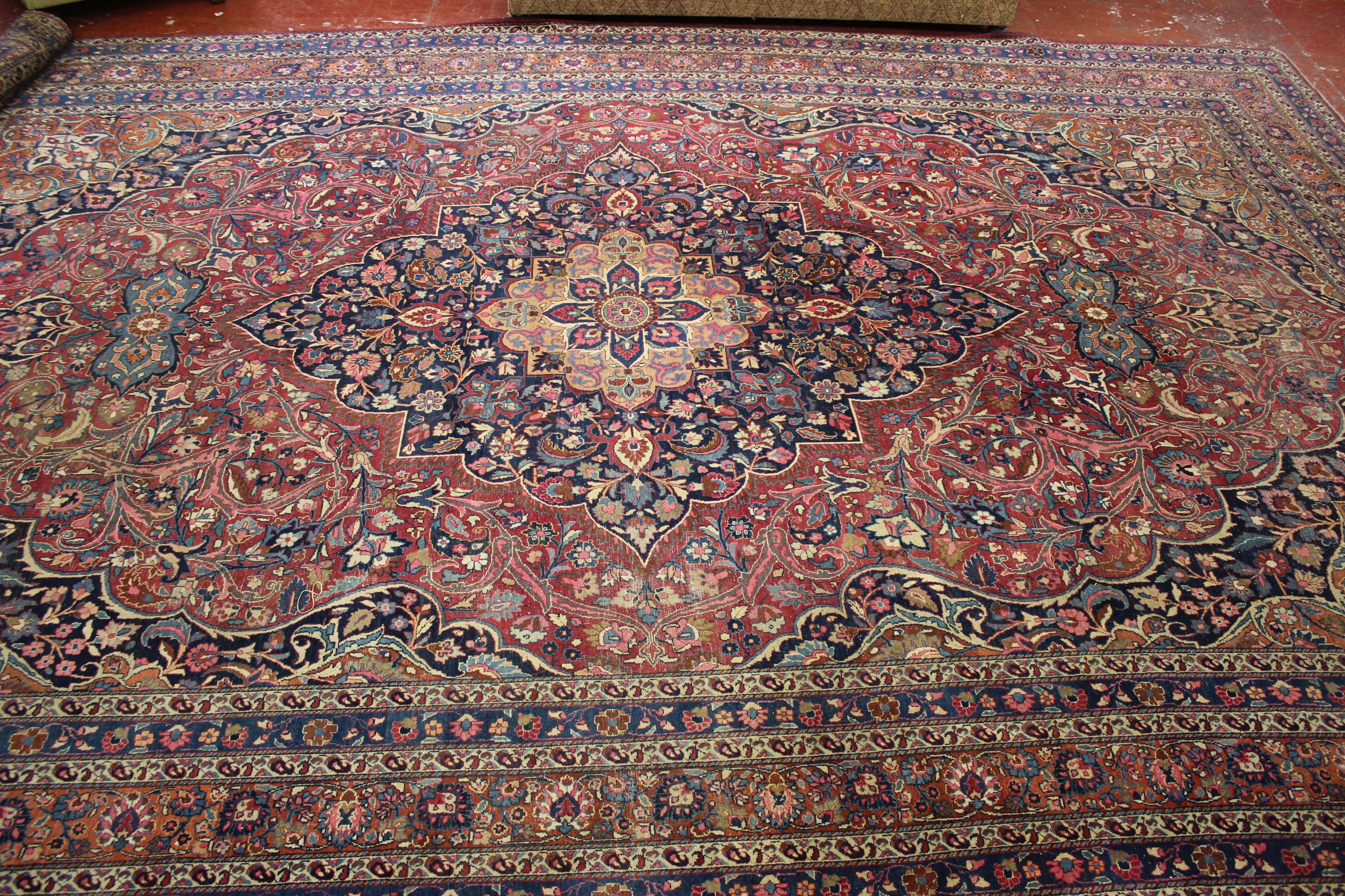 A Meshed carpet, the madder field with central indigo medallion within a floral border, bearing