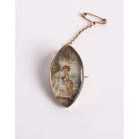 An 18th century gold and painted miniature brooch depicting a winsome lady seated beside a tree,