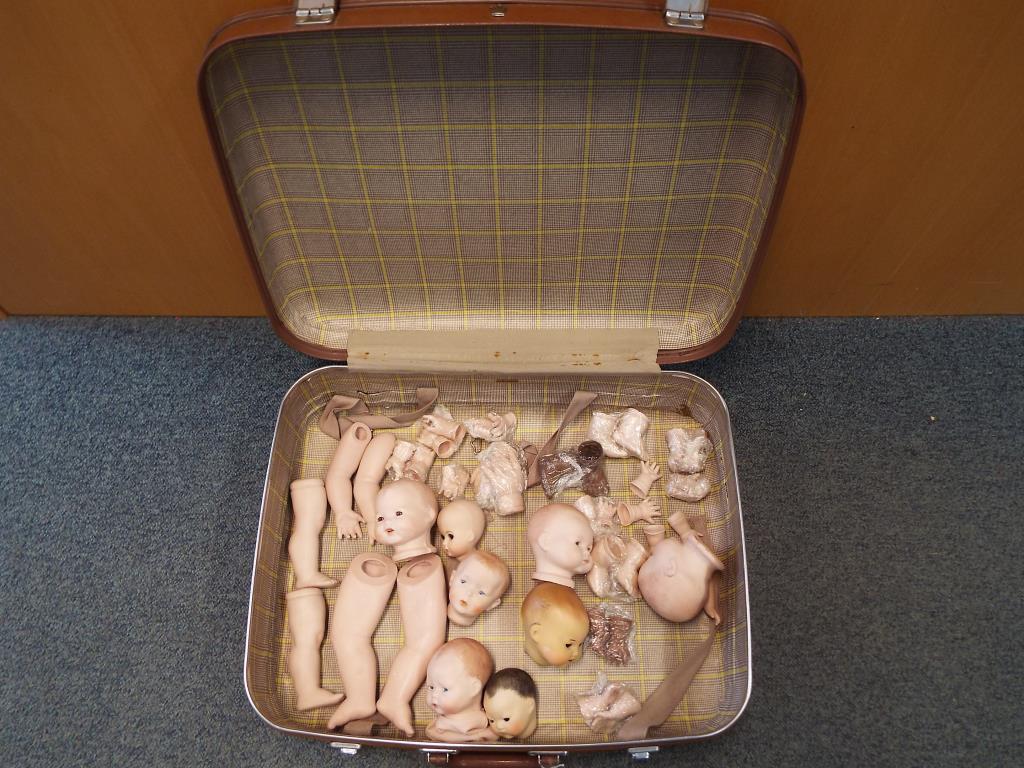 A vintage suitcase containing a quantity of modern heads and various doll's body parts