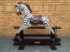 Rocking Zebra - a carved wooden rocking zebra with leather saddle and bridle on trestle base,