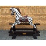 Rocking Zebra - a carved wooden rocking zebra with leather saddle and bridle on trestle base,