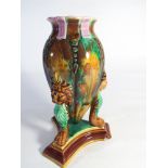 Majolica vase with lion mask handles and paw feet standing on a tripod base.