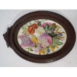 An oval porcelain plaque hand painted with summer flowers in a carved wooded frame height 24cms