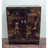 A Japanese black lacquer dwarf cabinet with a landscape scene picked out in relief to the doors