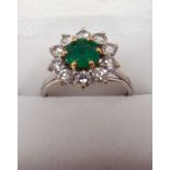 Emerald and diamond cluster ring, set with a circular emerald surrounded by brilliant cut diamonds,