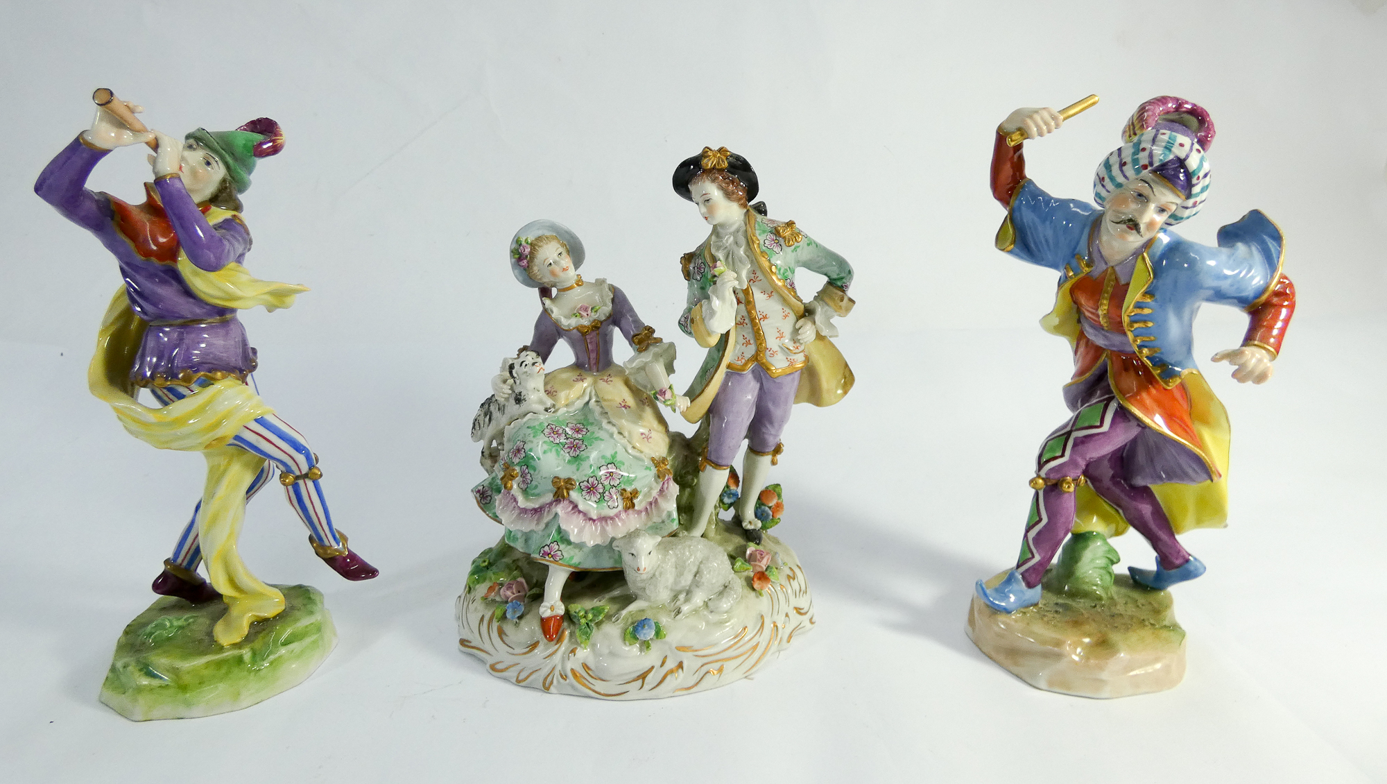 Two Dresden porcelain figurines of court jesters and a pastoral group of shepherd and shepherdess